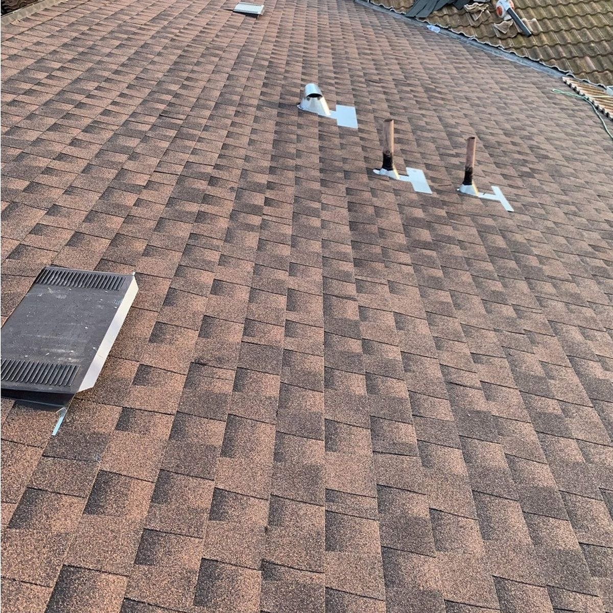 Brown shingle roof with vents, skylight, and small roof penetrations near the ridge