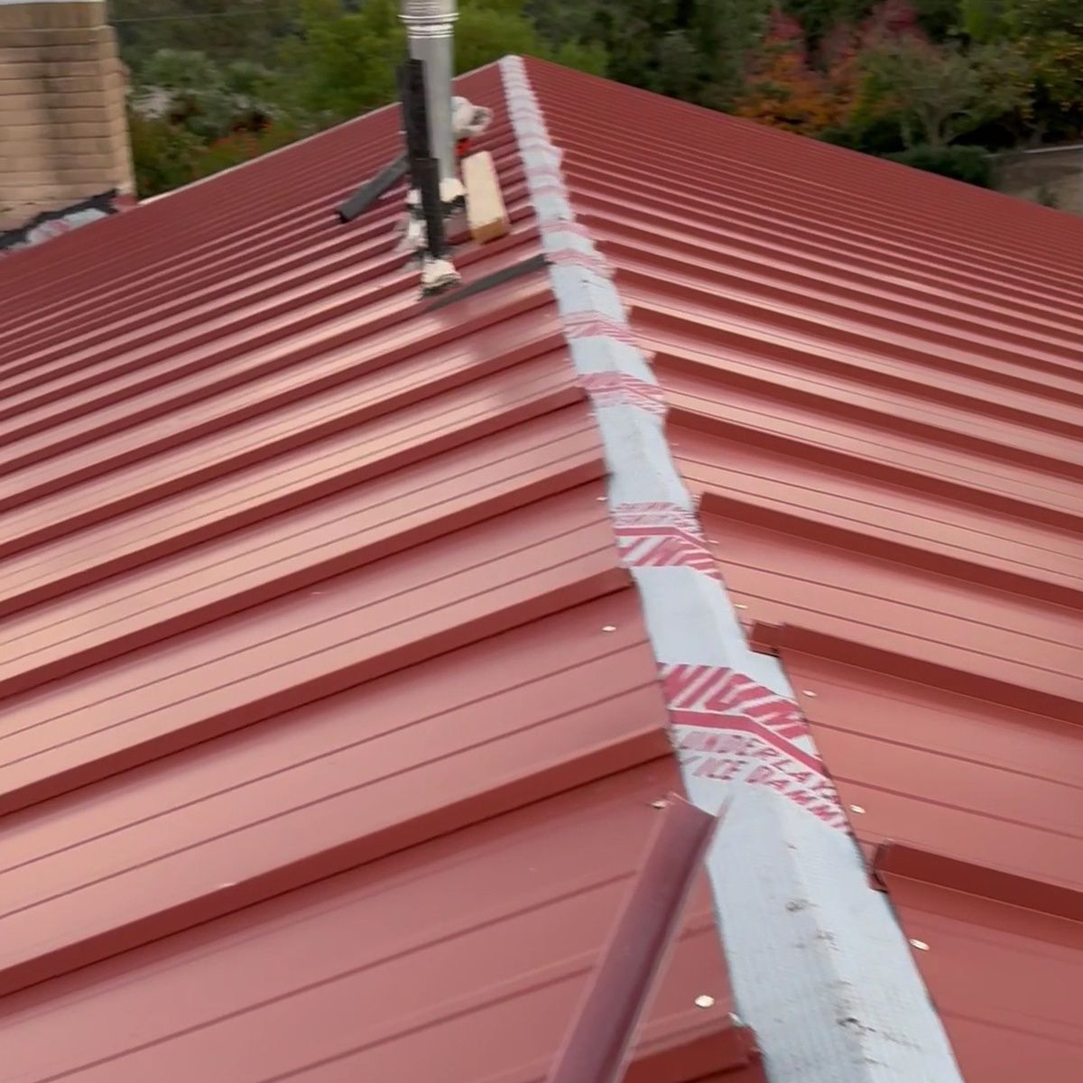 Red metal roof with a central seam and roof vent, viewed from above.