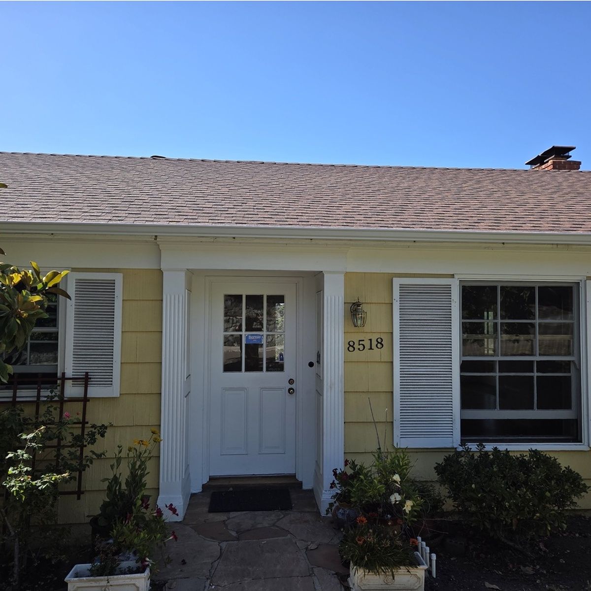 Front entrance of a yellow house with white door, shutters, and a stone walkway under a blue sky