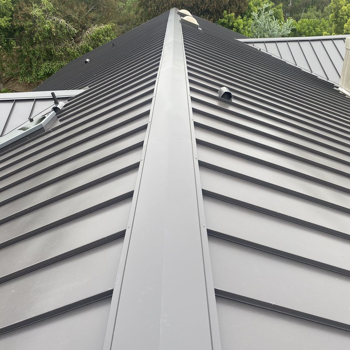 Metal roof viewed from below, with a central ridge and gray panels leading toward the peak.
