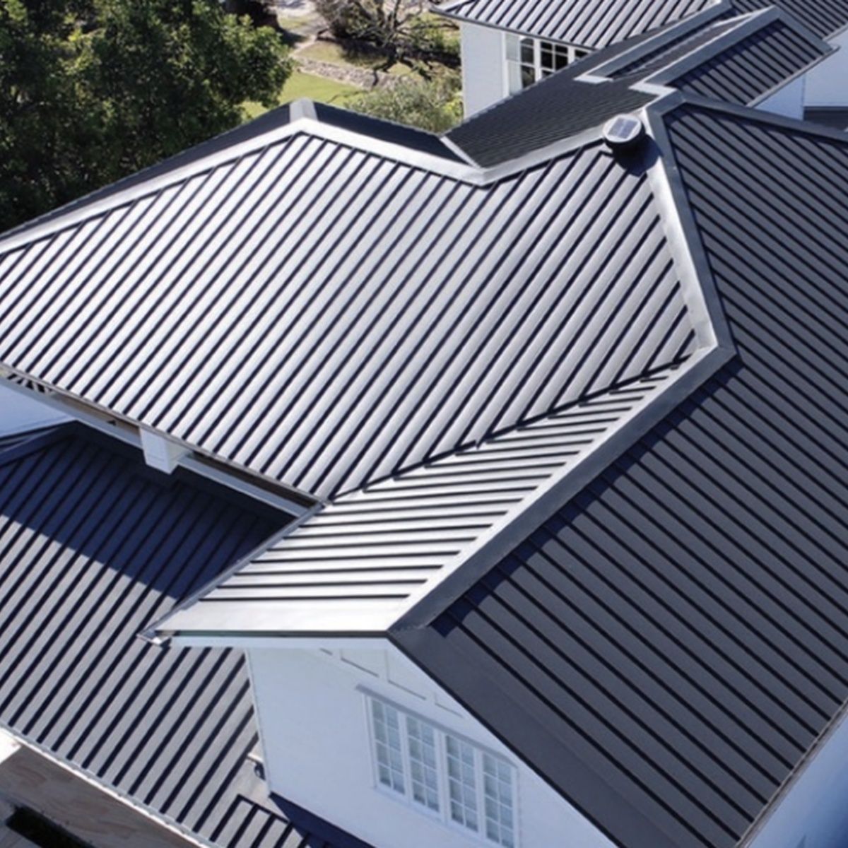 Aerial view of a house with dark metal roofs and white trim, showing multiple roof sections and skylights