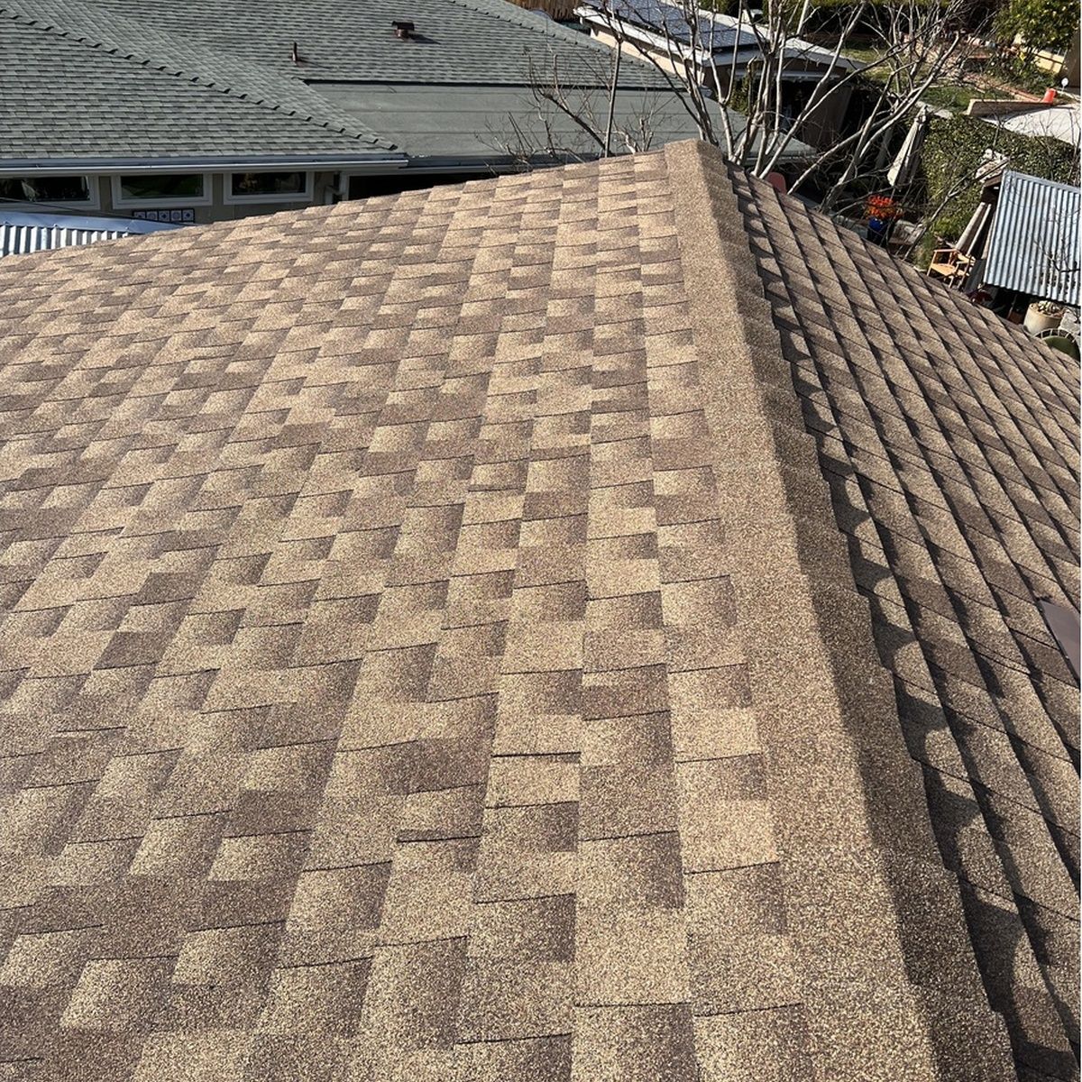 Close-up of a brown shingled roof with a ridge line and rooftops in the background.