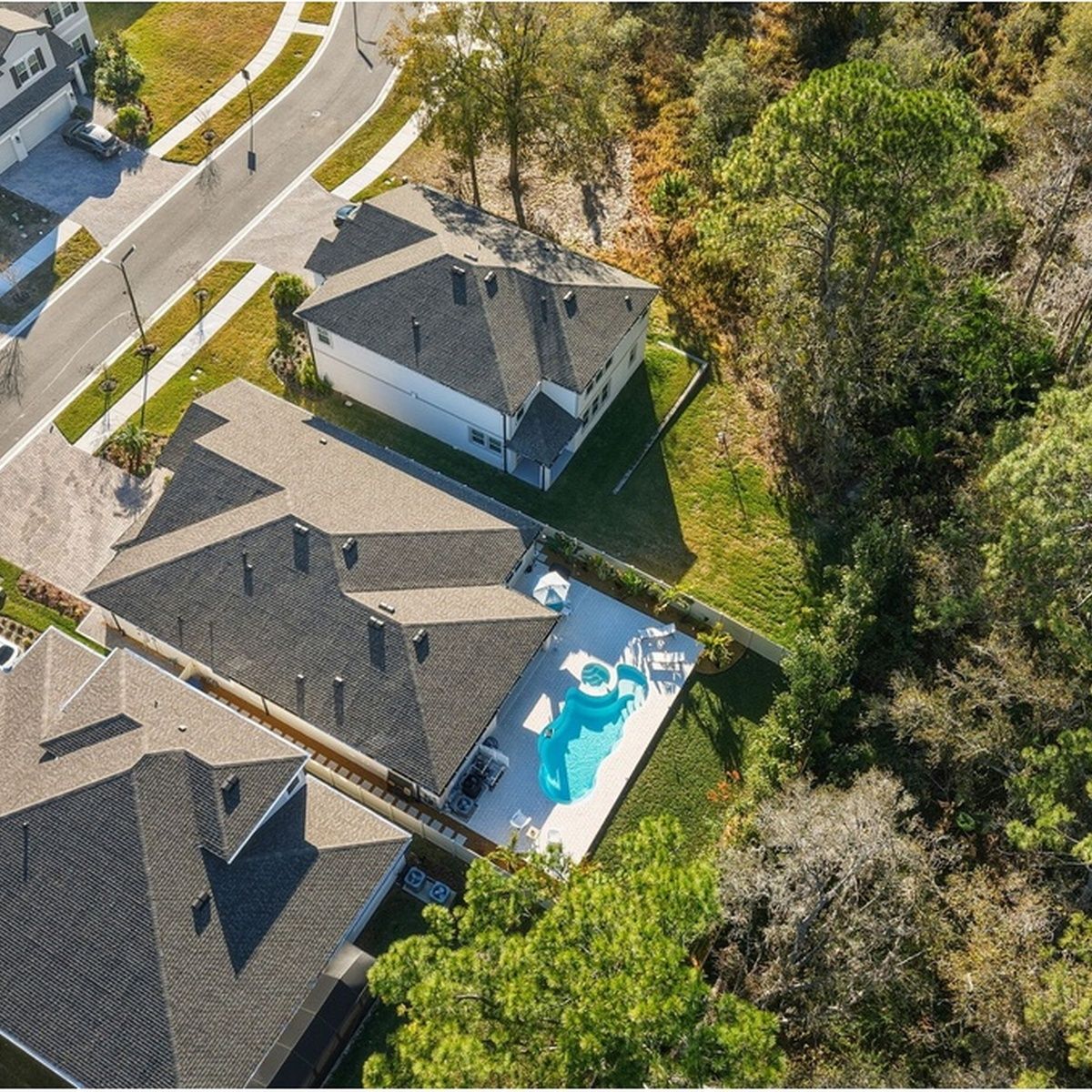 Aerial view of suburban houses with a backyard pool and surrounding trees.