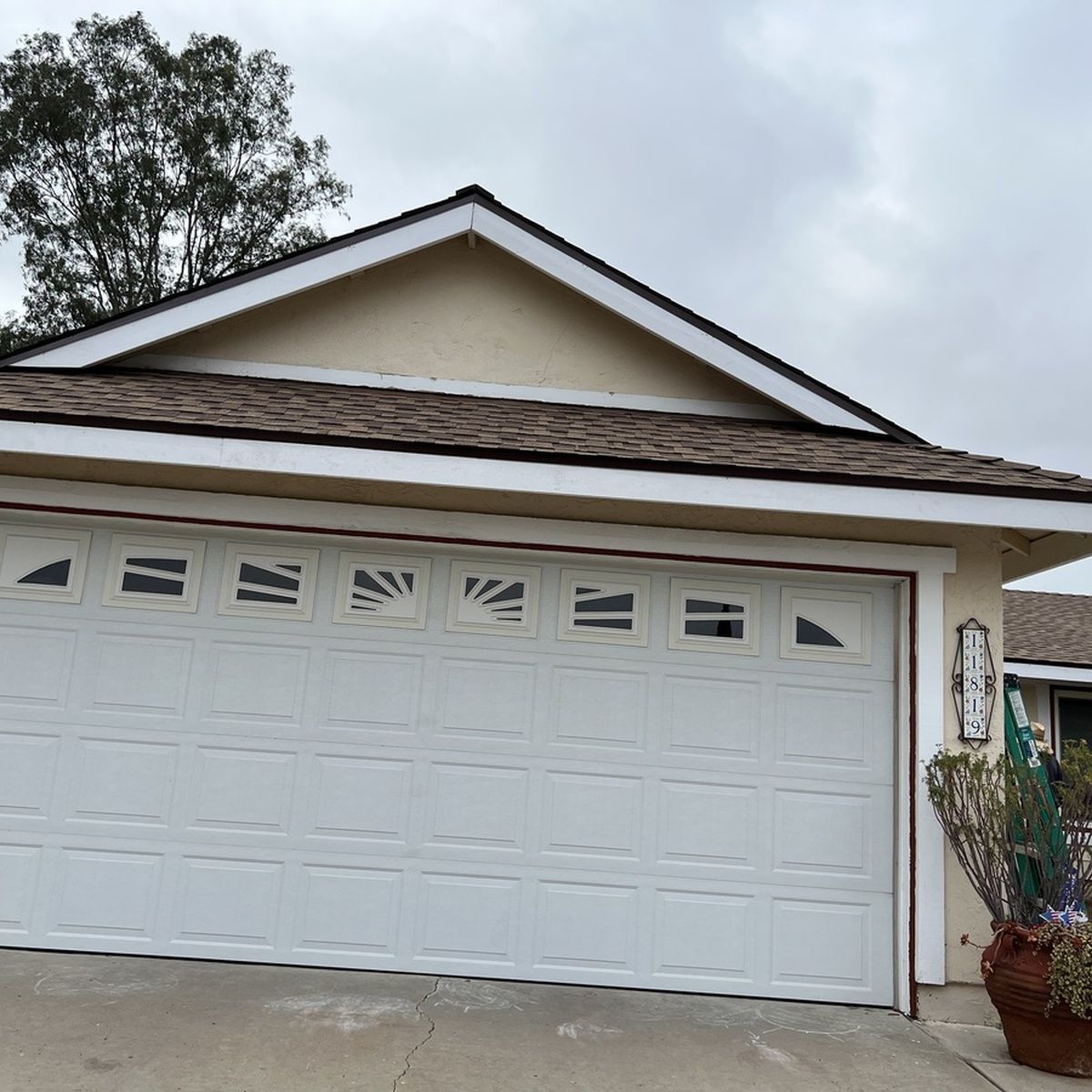 White garage door on a beige house with brown roof and cloudy sky
