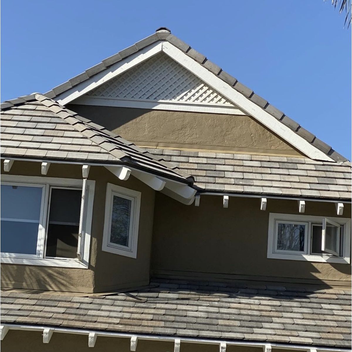 House roof with gray shingles and white trim against a clear blue sky