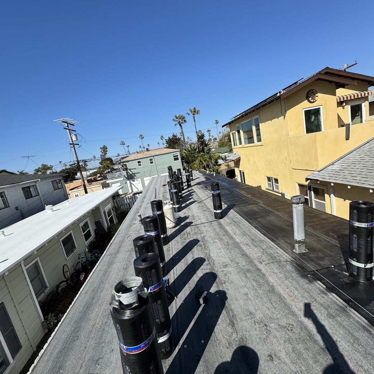 Rooftop walkway with black vents and a yellow building under a clear blue sky.