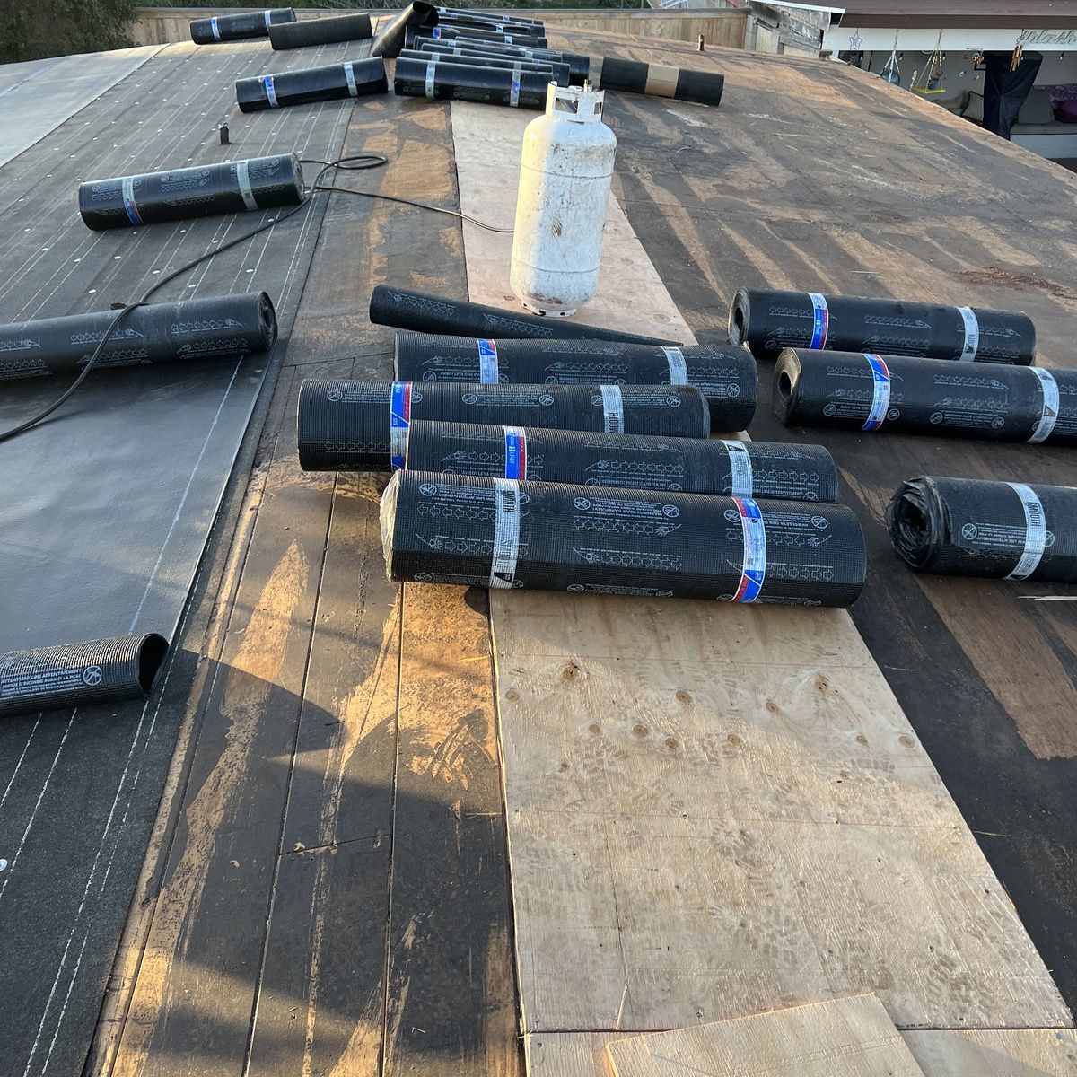 Rolls of black roofing material scattered across a flat roof near a white vent pipe.