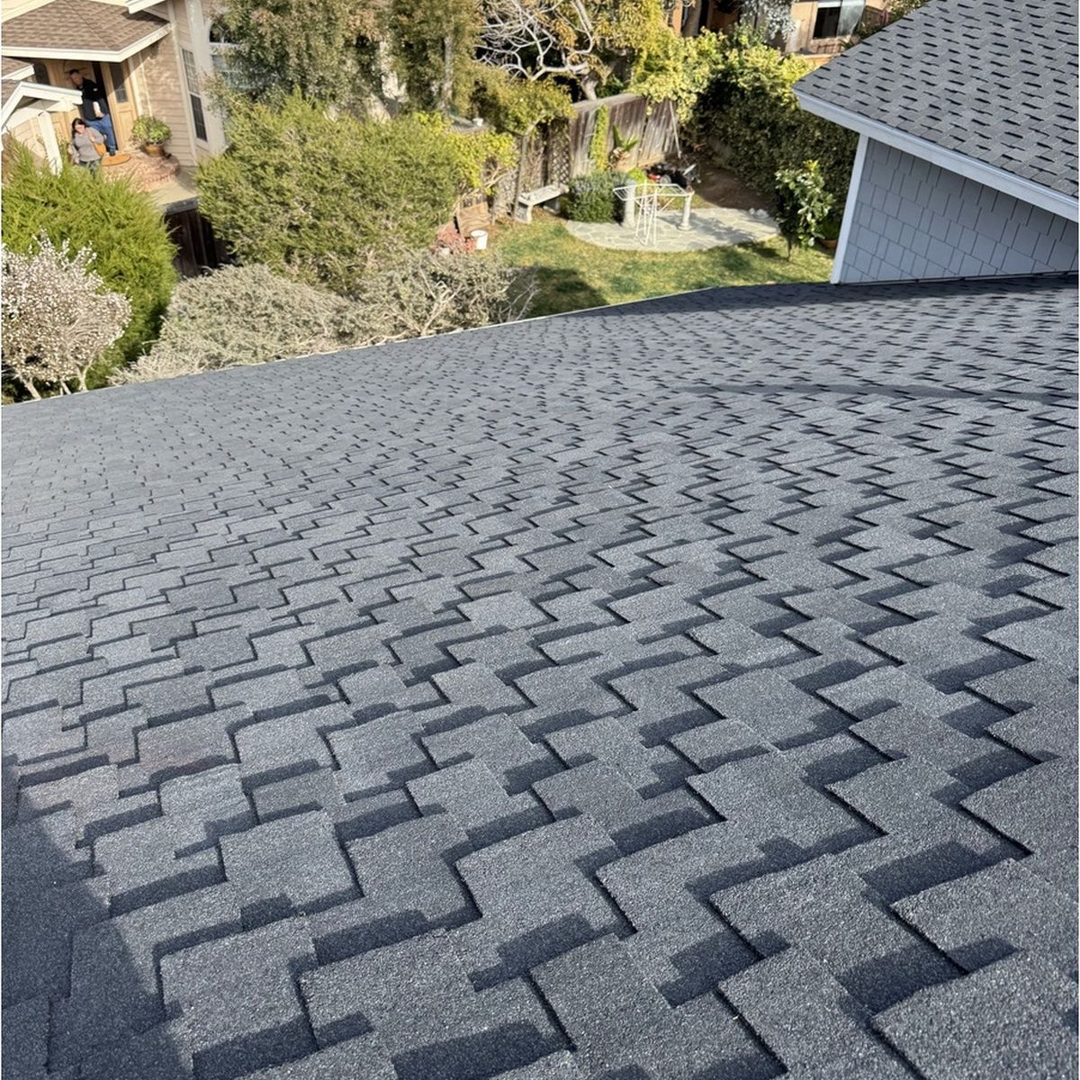 Gray shingle roof with zigzag pattern, viewed from above, with trees and houses in the background