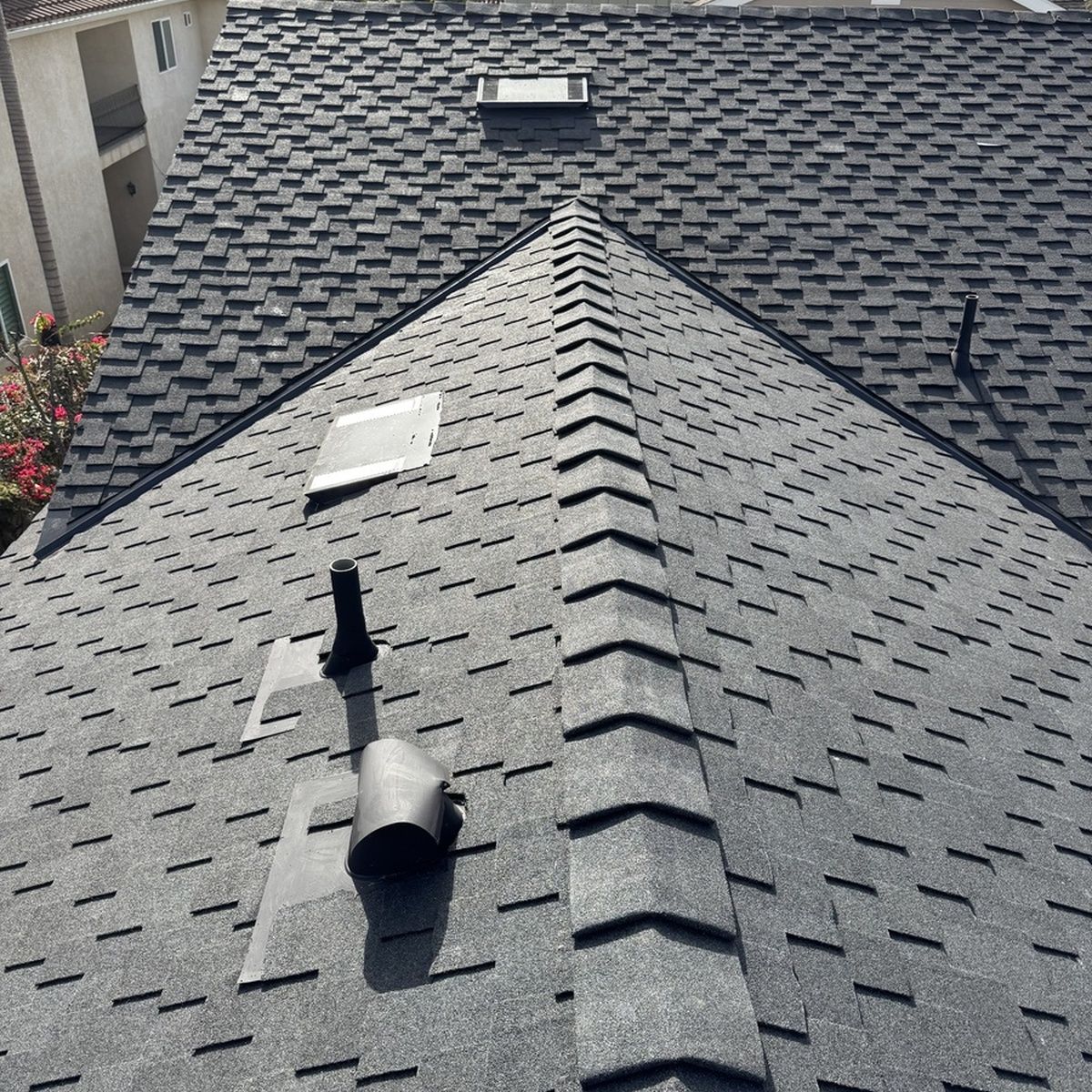 Gray shingled roof with ridge vents, a skylight, and a chimney in bright sunlight.