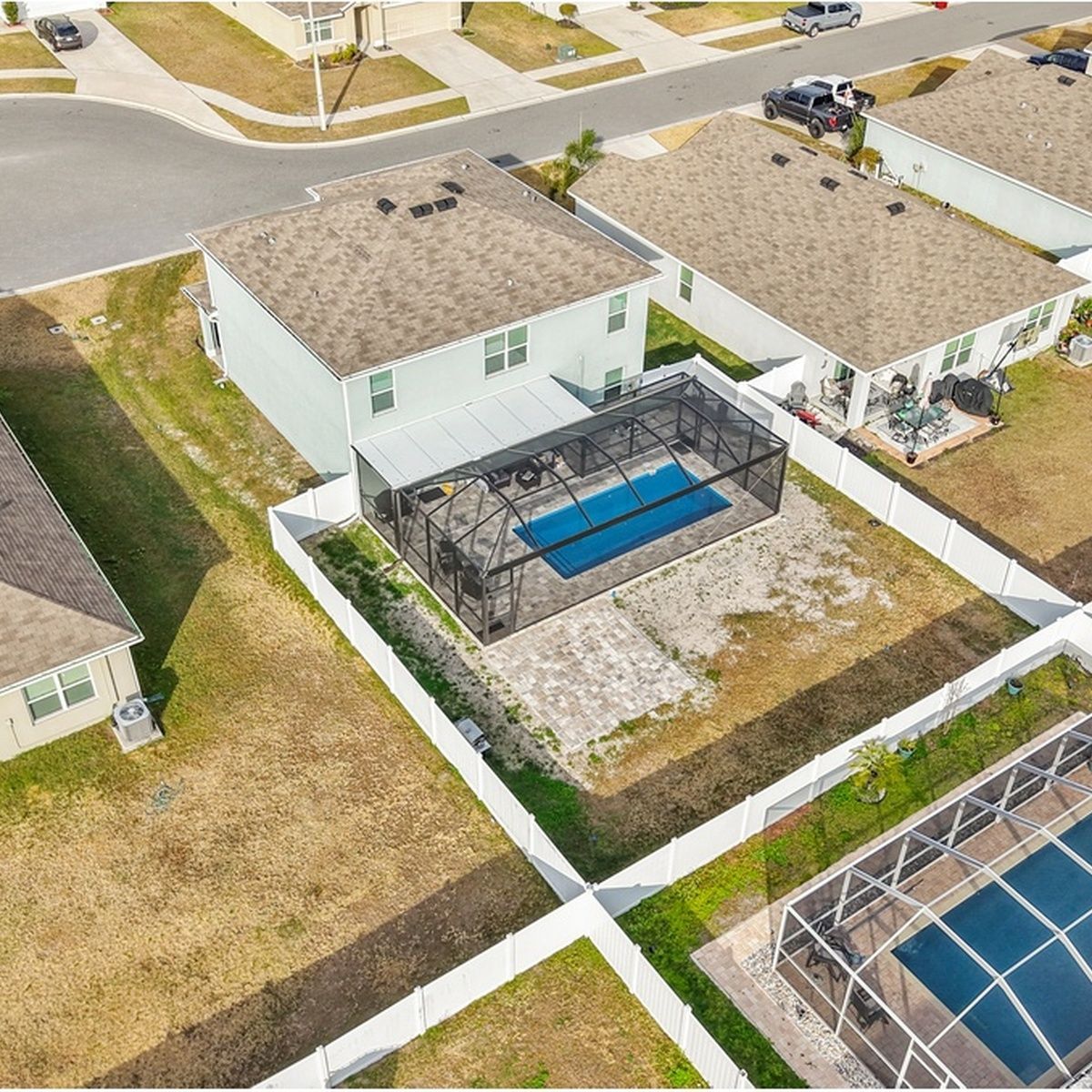 Aerial view of suburban homes with fenced backyards and a blue screened-in pool.