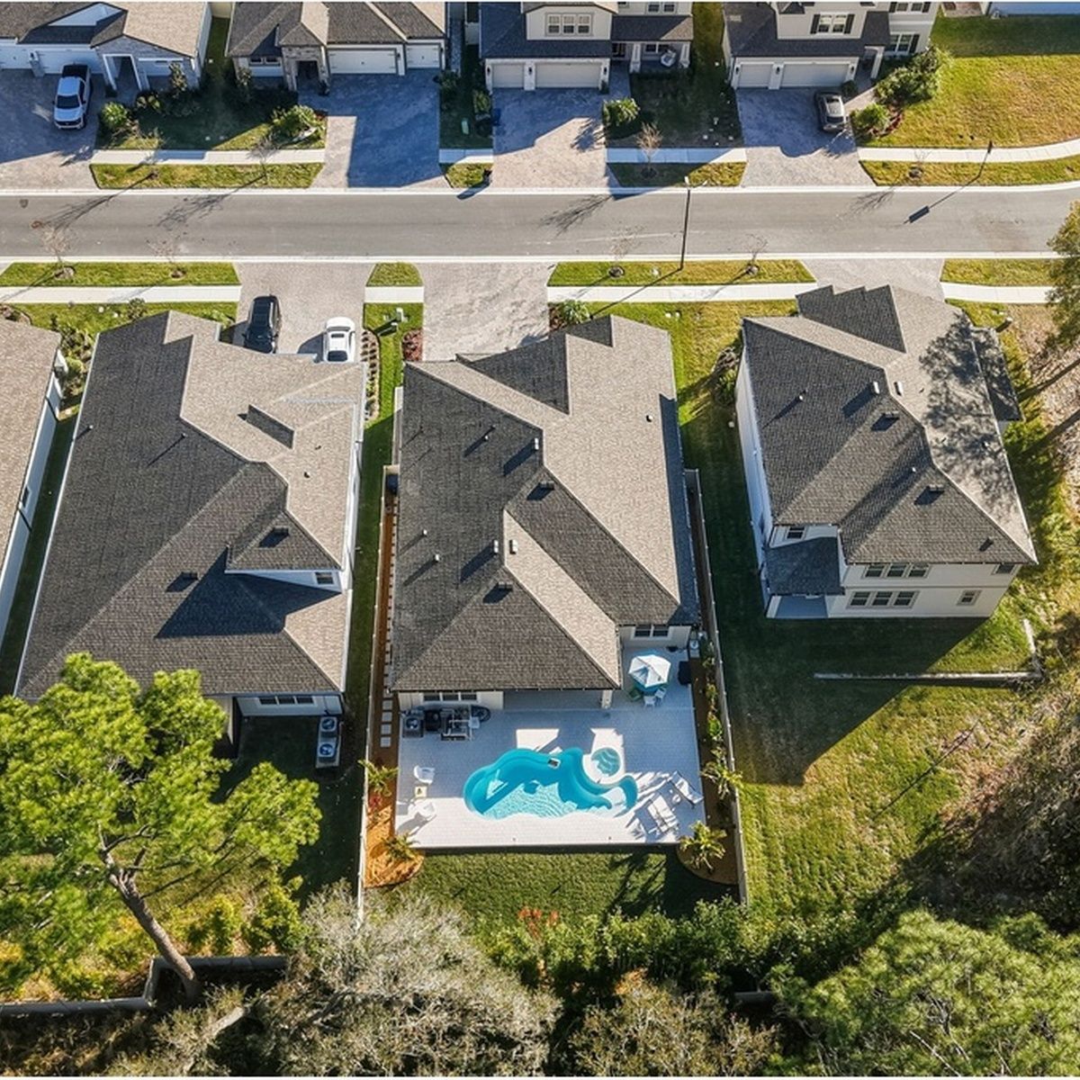 Aerial view of three suburban homes with a backyard pool and a street at the top.