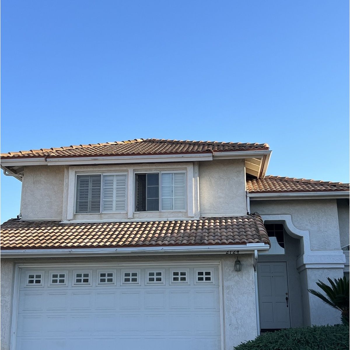 Two-story suburban house with a white garage and terracotta roof under a clear blue sky