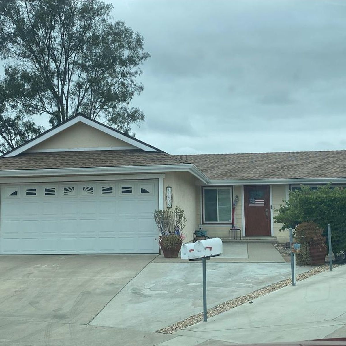 Single-story suburban house with a two-car garage, front porch, and desert landscaping under a cloudy sky