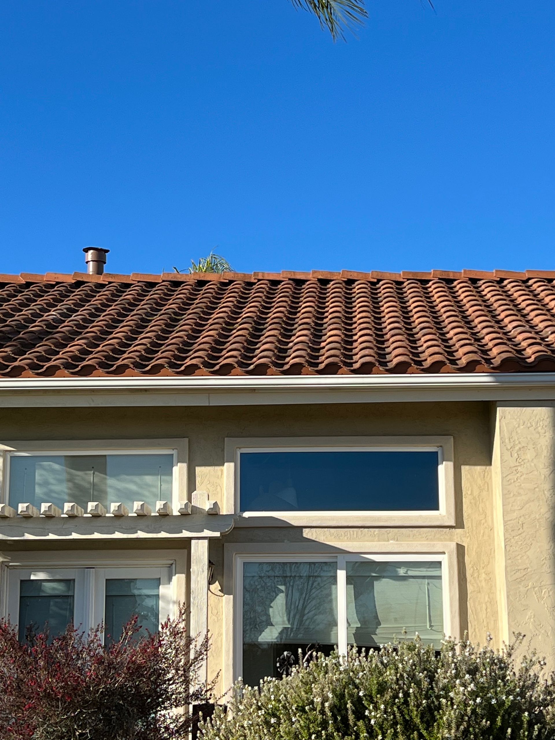 Sunlit beige house with red tiled roof and large windows under a clear blue sky