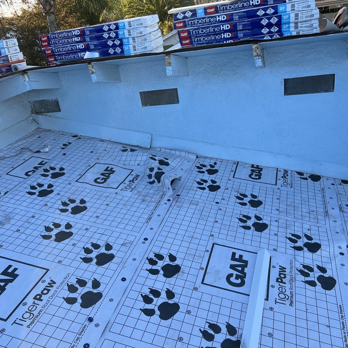 Roofing underlayment with black paw-print patterns on a sloped roof, beneath stacked materials.