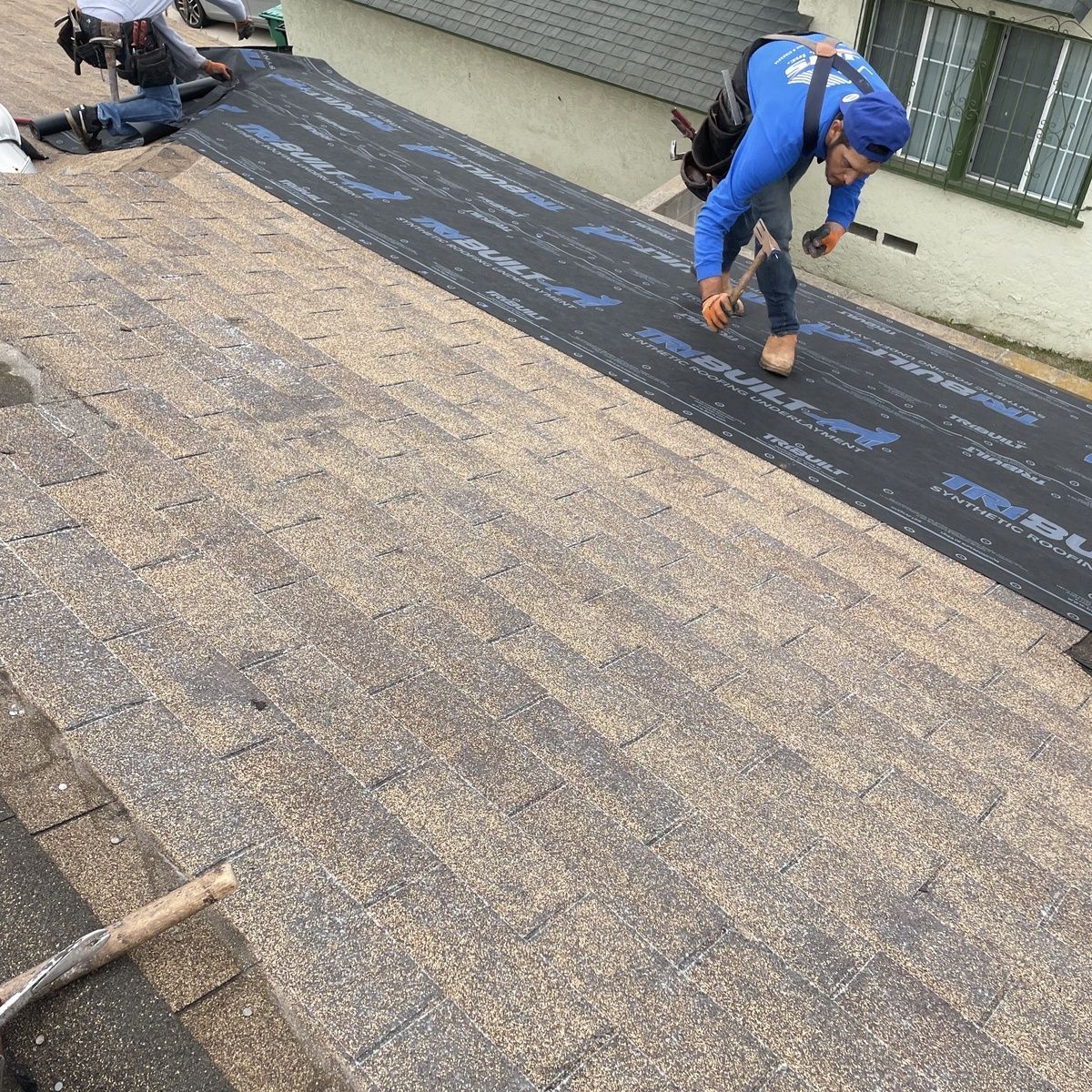 Workers installing roofing underlayment on a sloped roof with shingles partially removed