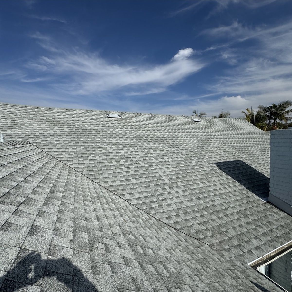 Gray shingled roof under a blue sky with wispy clouds and a roof vent at right
