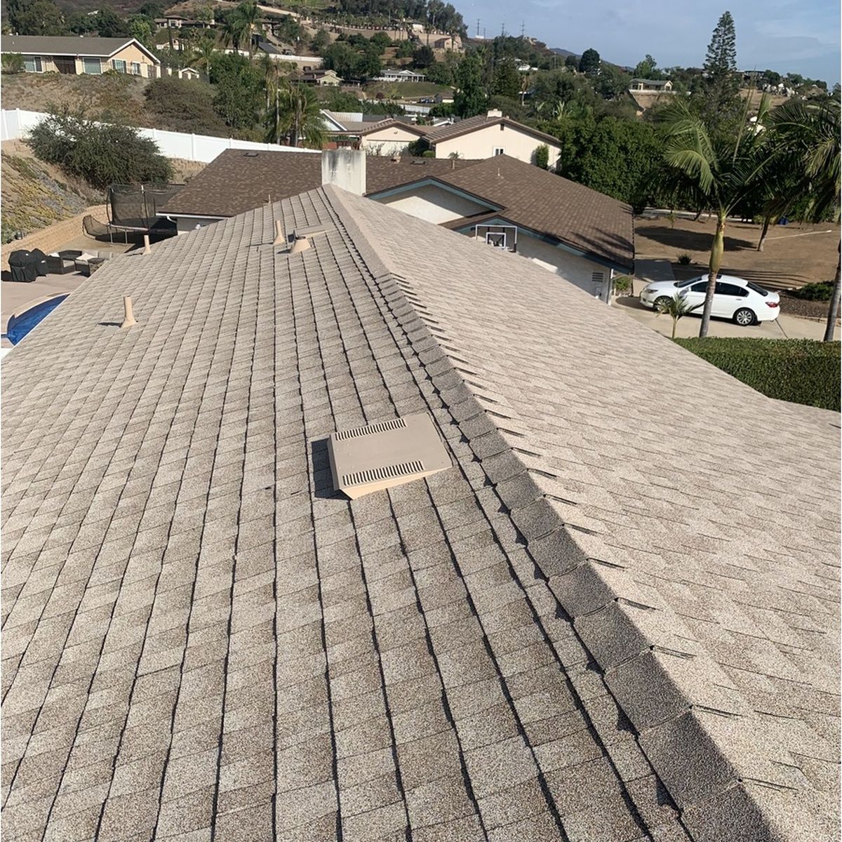 Rooftop covered in light gray shingles with vents, overlooking a suburban neighborhood on a sunny day
