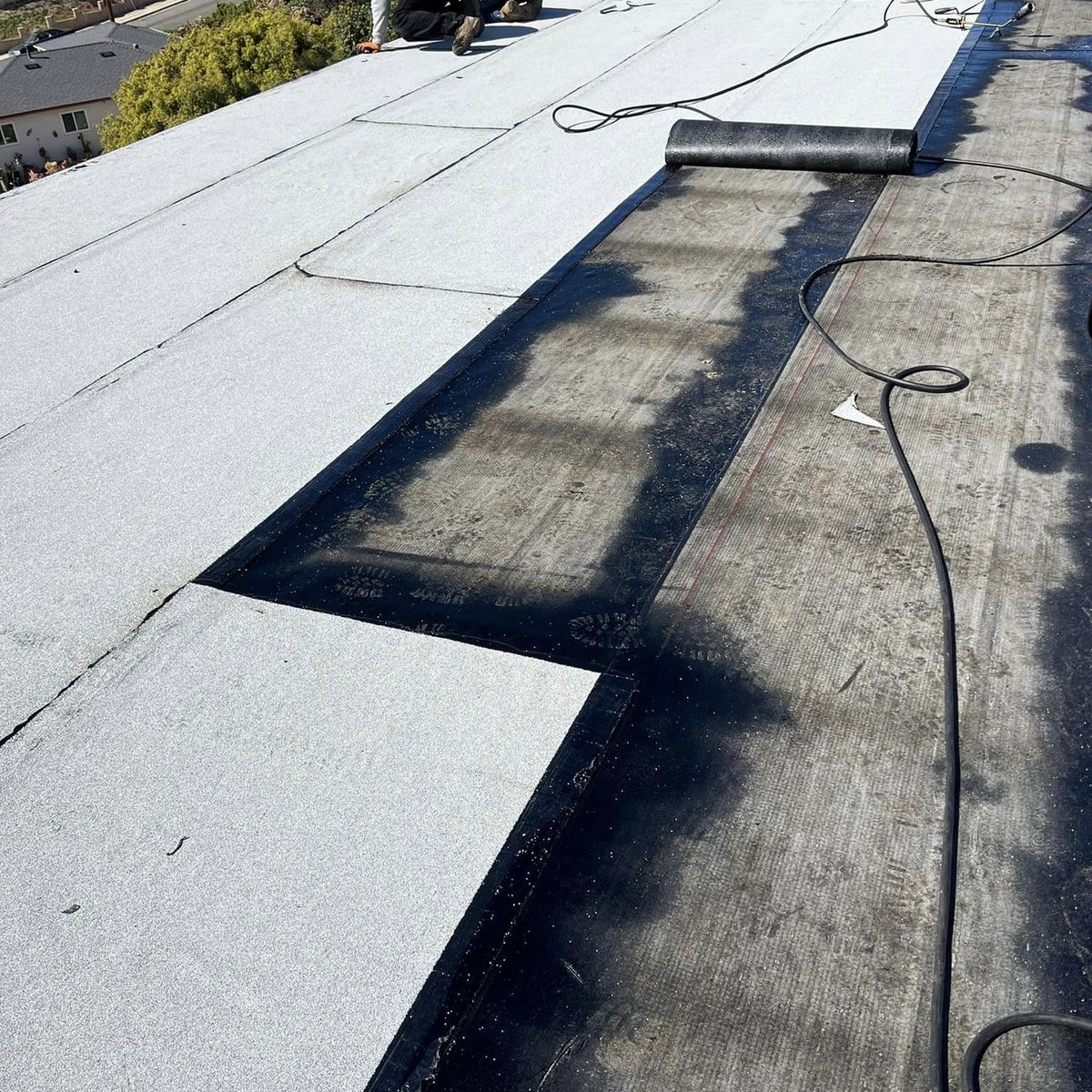Rooftop with white coating and a dark repaired section beside a rolled roof membrane.