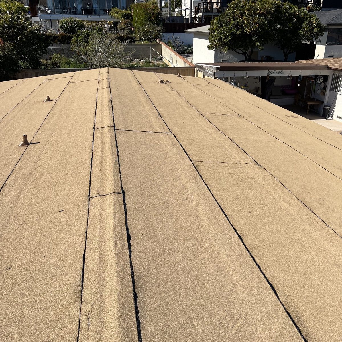 Rooftop with tan gravel surface and dark seam lines, overlooking nearby buildings and trees