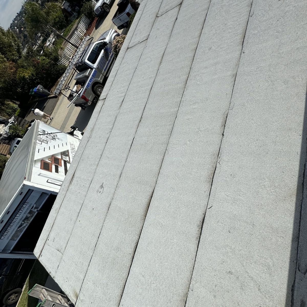 Tilted view of a gray shingle roof with parked cars and trees in the background