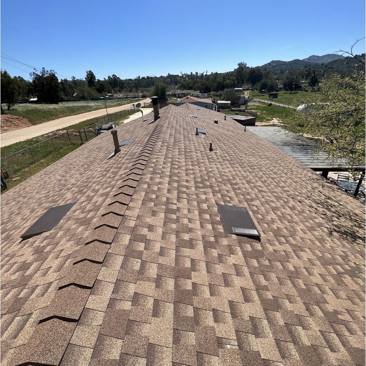 Rooftop covered in brown shingles with vents and a person working under a clear blue sky.