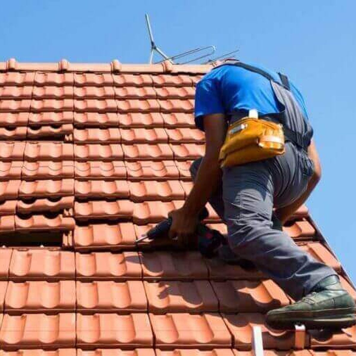 Worker in blue shirt repairing terracotta roof tiles with a power tool.
