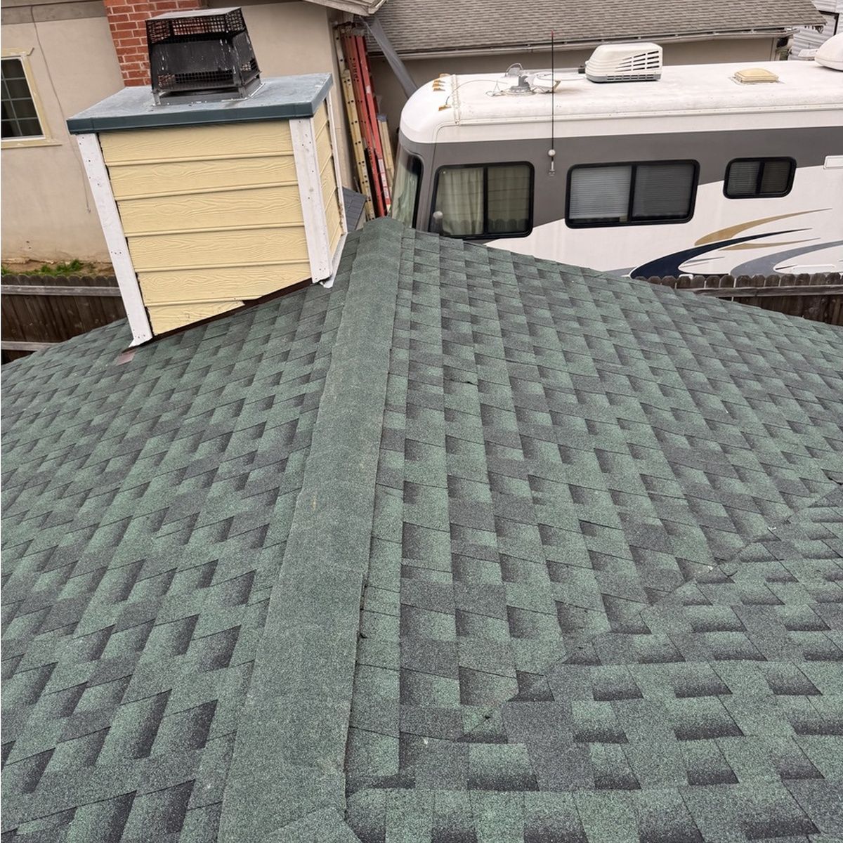 Green shingled roof with a ridge peak, beside a camper and a small shed.