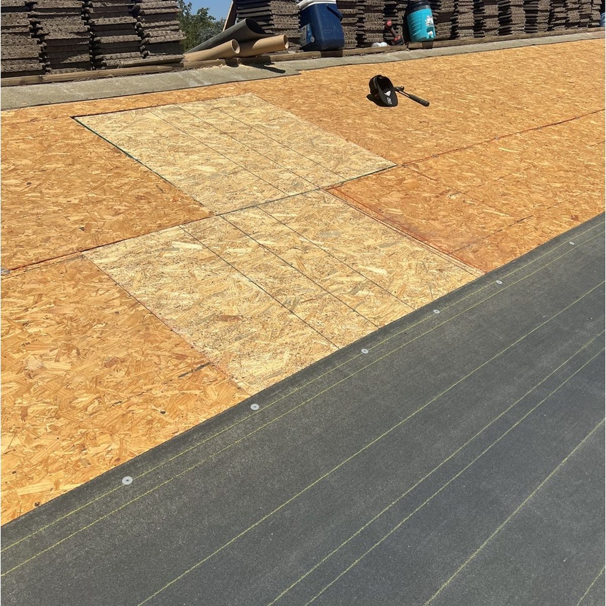 Construction site with OSB panels on a roof deck and a tool near stacked materials in the background
