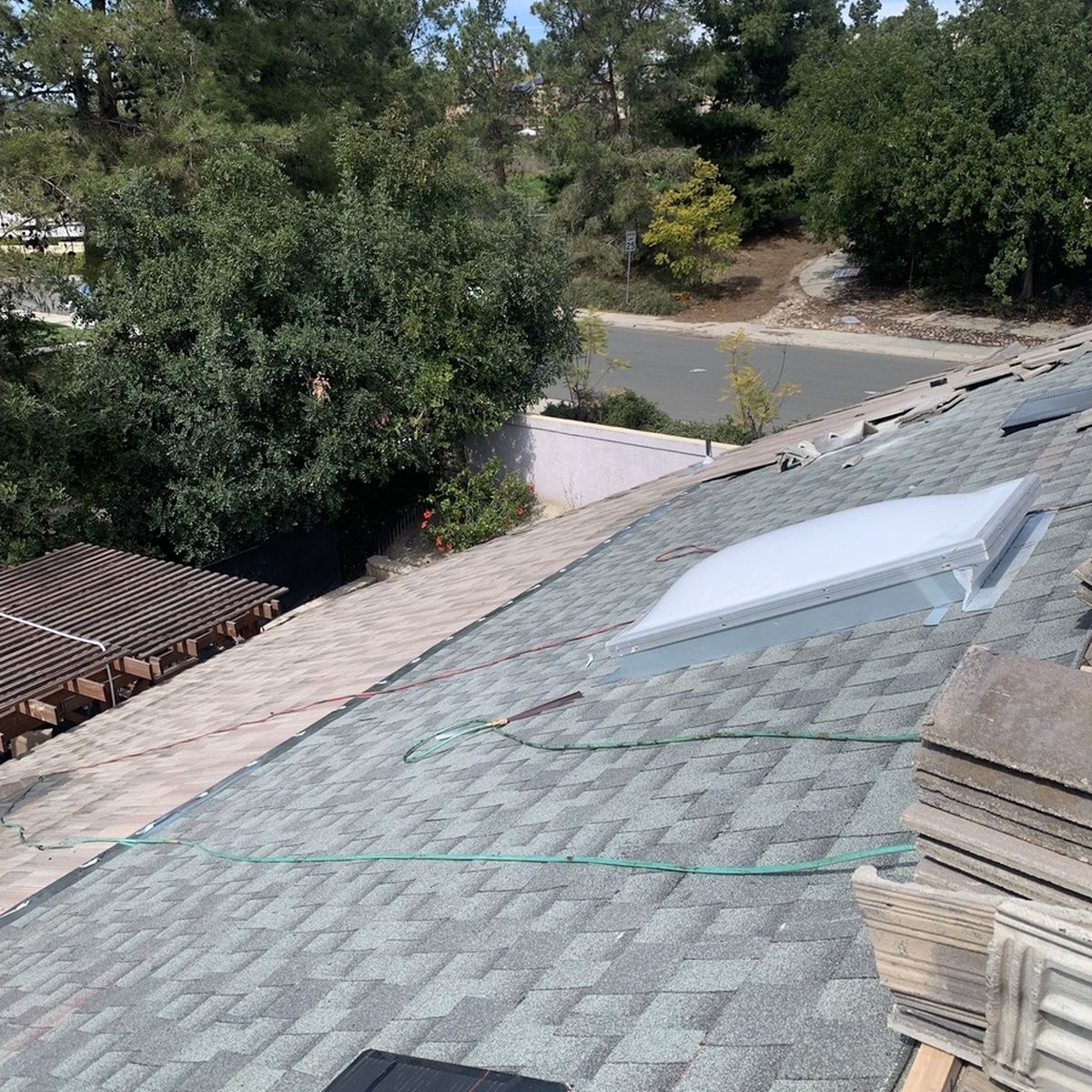 Rooftop with gray shingles and skylight beside trees and a driveway below