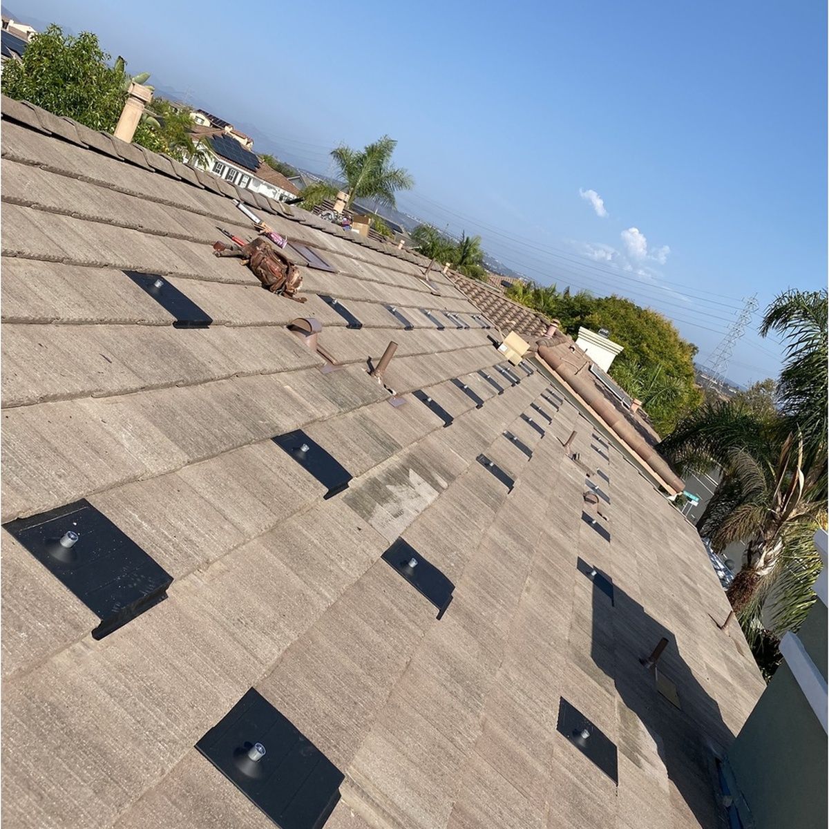 Sloped rooftop with brown shingles and black vents under a clear blue sky.