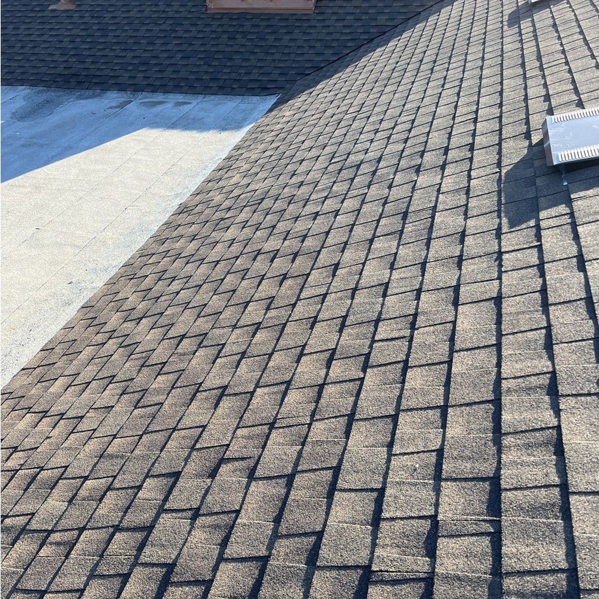 Sloped roof covered in gray shingles with sunlight and a small rooftop vent.