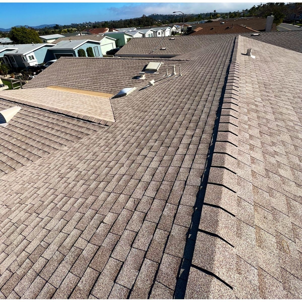 Rooftops with brown and tan shingle sections viewed from above on a sunny day.