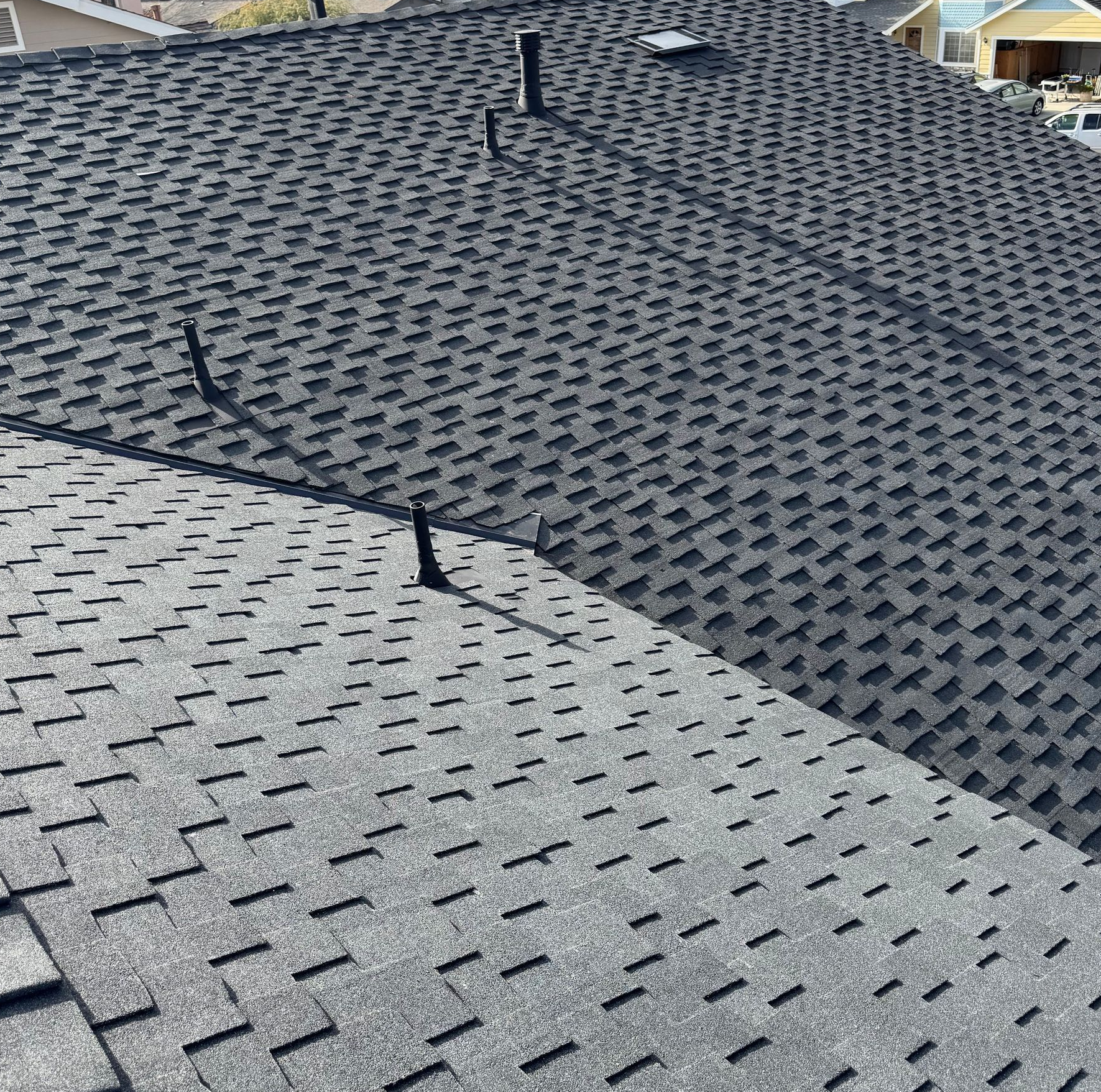 Close-up of a shingled roof with several black vent pipes on a sloped surface.