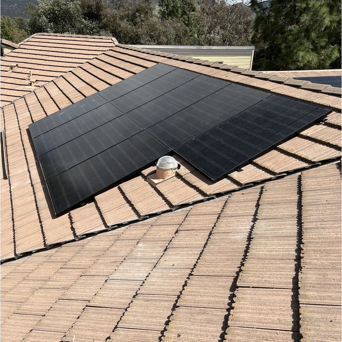 Black solar panels mounted on a tan shingled roof with a rooftop vent in the center.