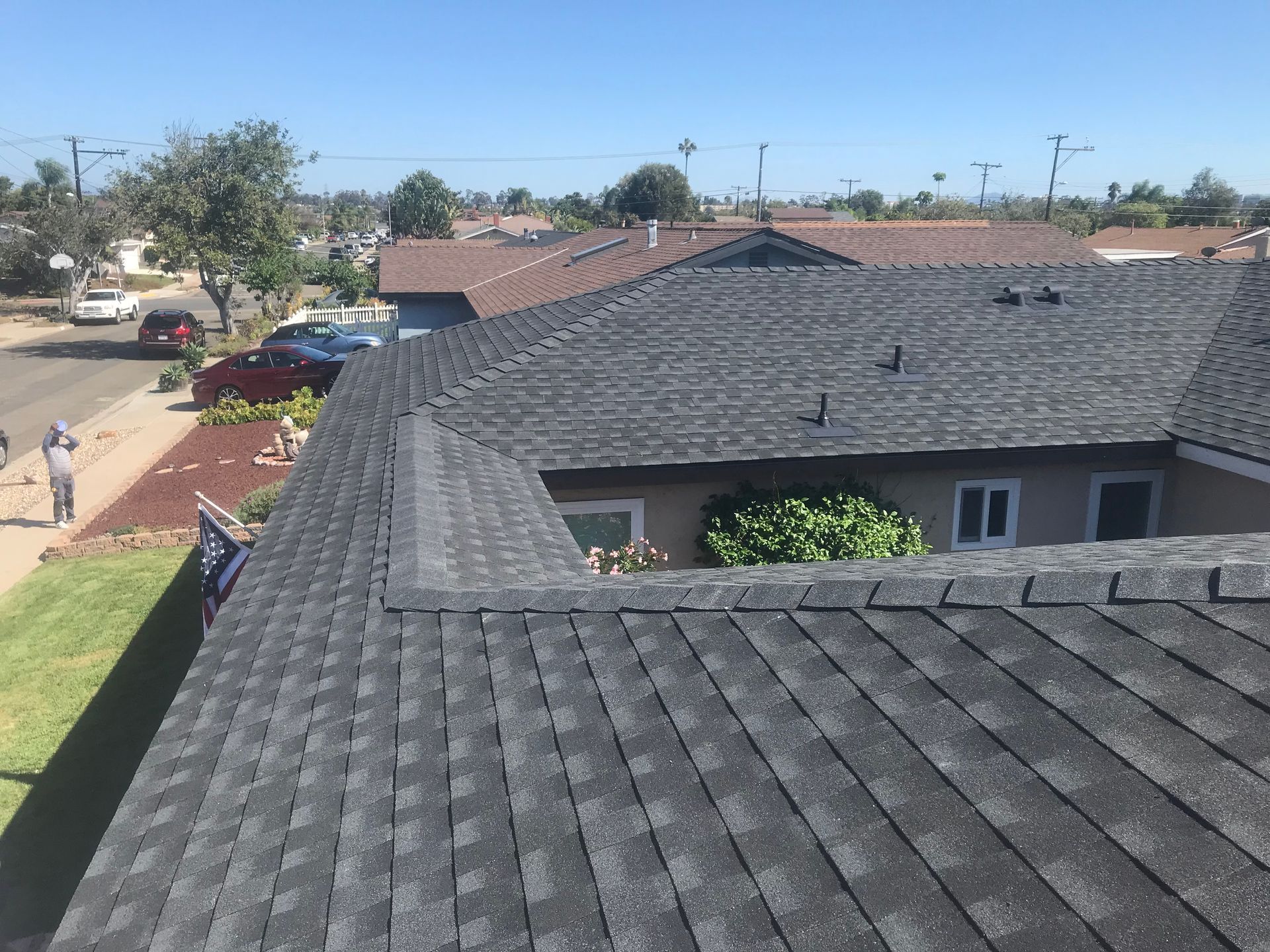 View from a rooftop over suburban houses, a street, and parked cars under a clear blue sky