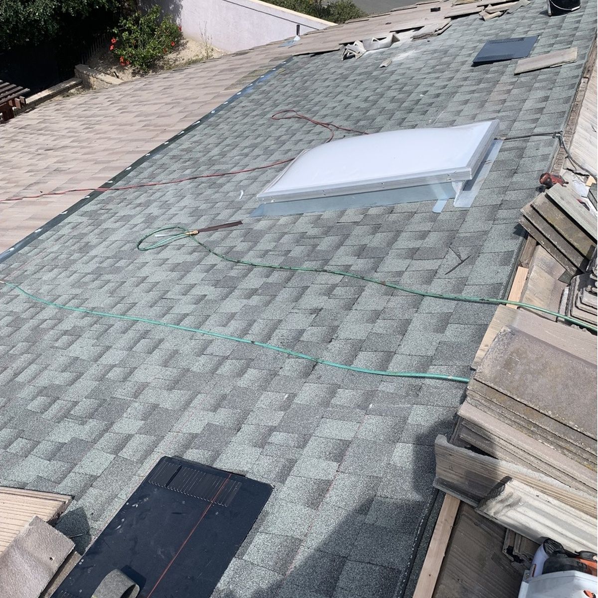 Tilted view of a shingled roof with two skylights and stacked roof tiles along the edge