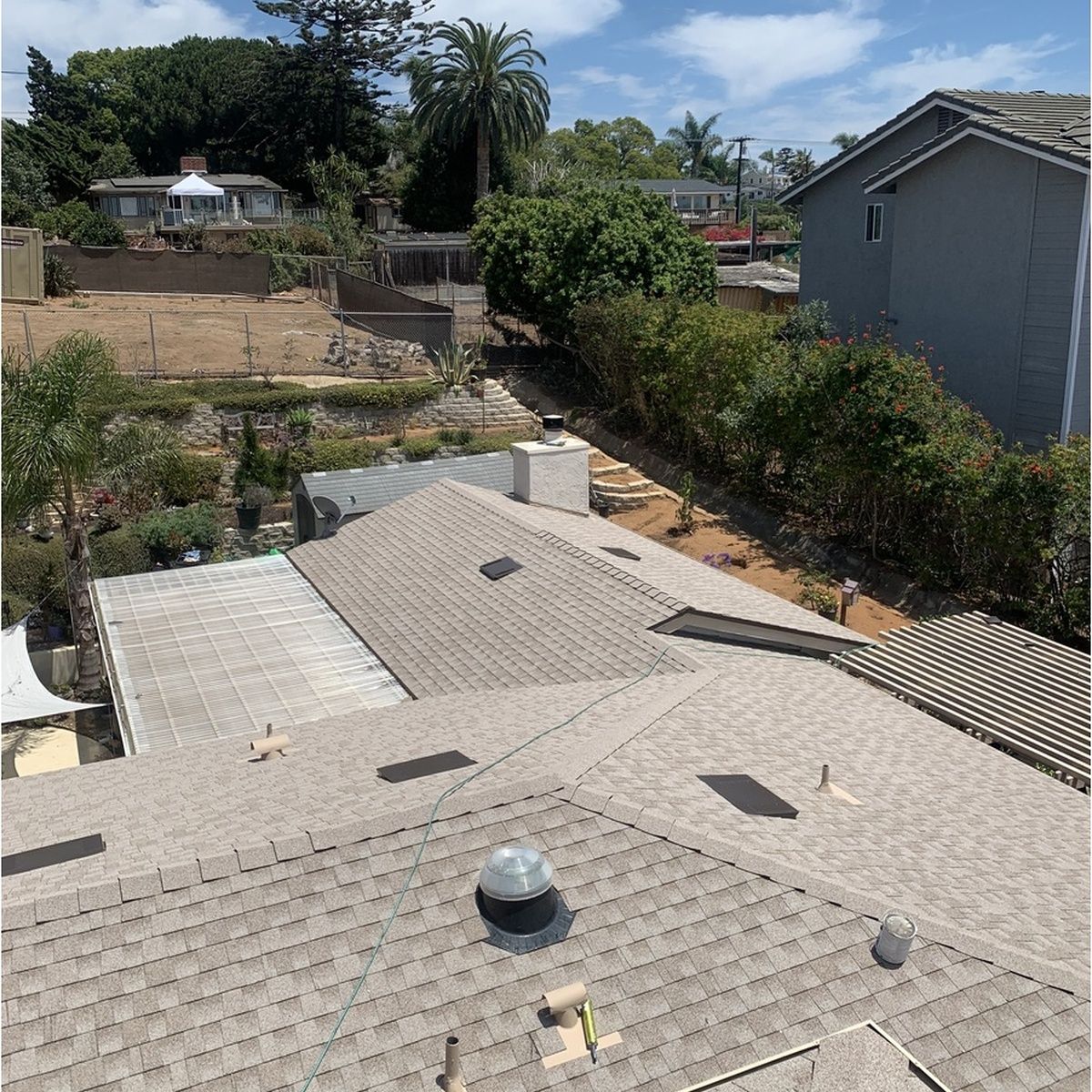 Rooftops and a backyard with hedges, trees, and a partly cloudy sky