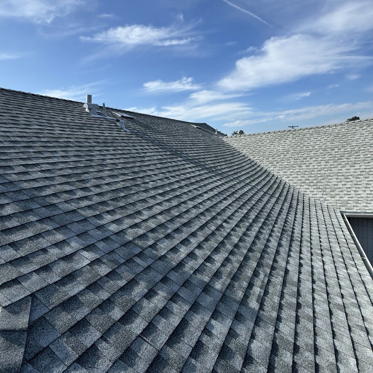 Gray shingled rooftops under a blue sky with wispy clouds