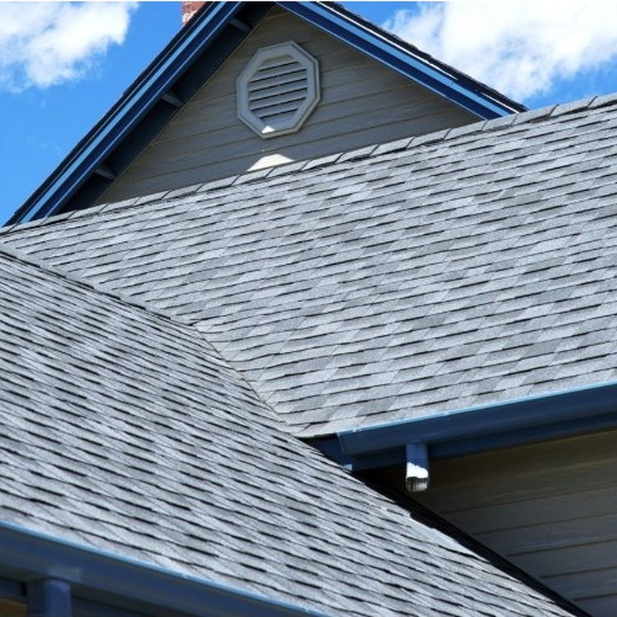 Blue-trimmed house roof with gray shingles and an attic vent under a clear sky
