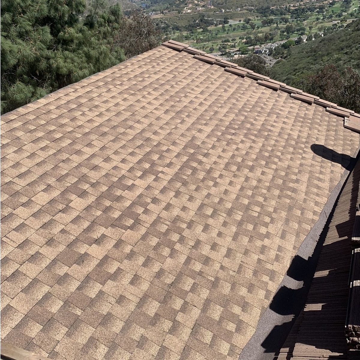 Brown shingled roof overlooking a green valley and hillside деревы