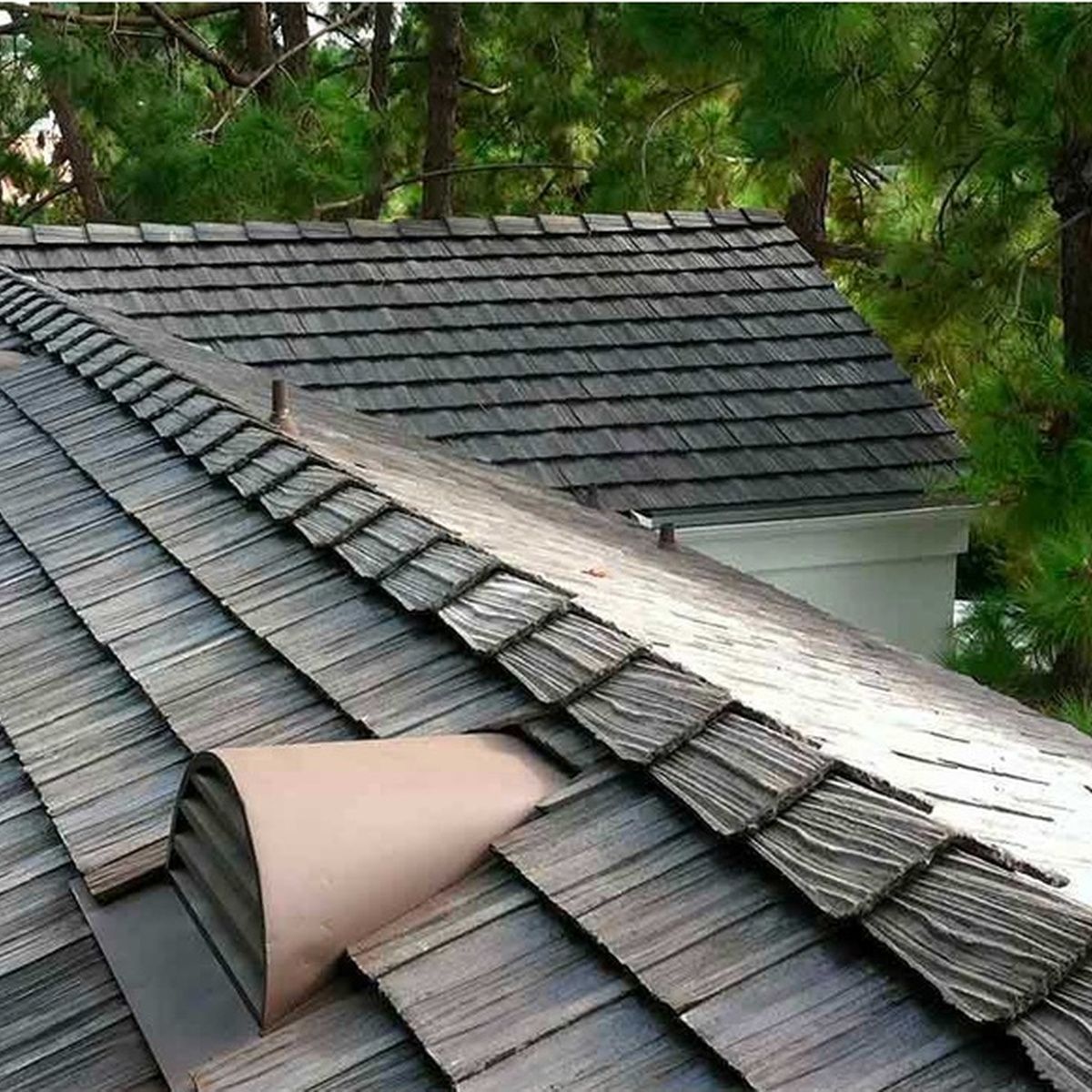 Damaged gray shingle roof with a curled-up section exposing the underlayment