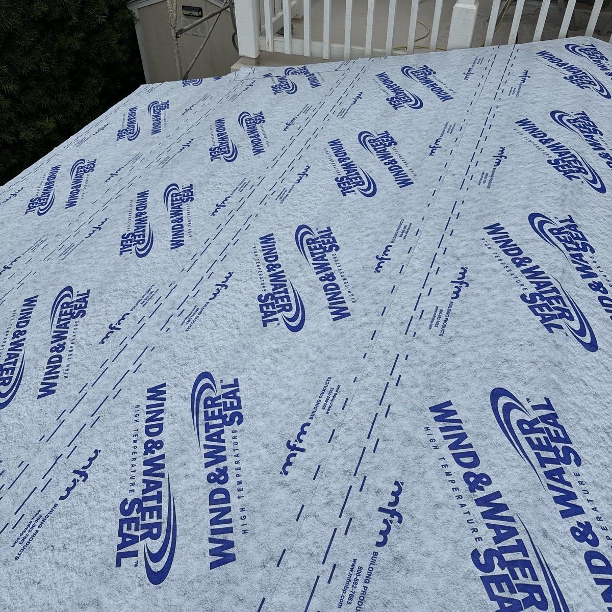 Blue-and-white protective roof underlayment stretched over a sloped roof near white railings