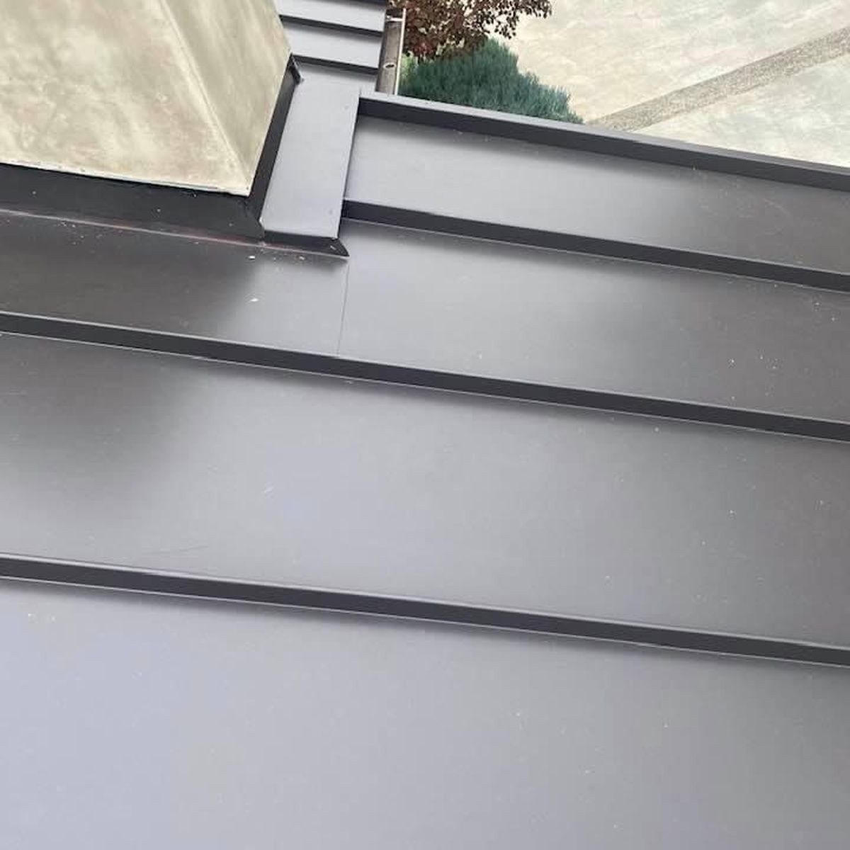 Gray metal roof panels meeting a wall with a rooftop vent pipe