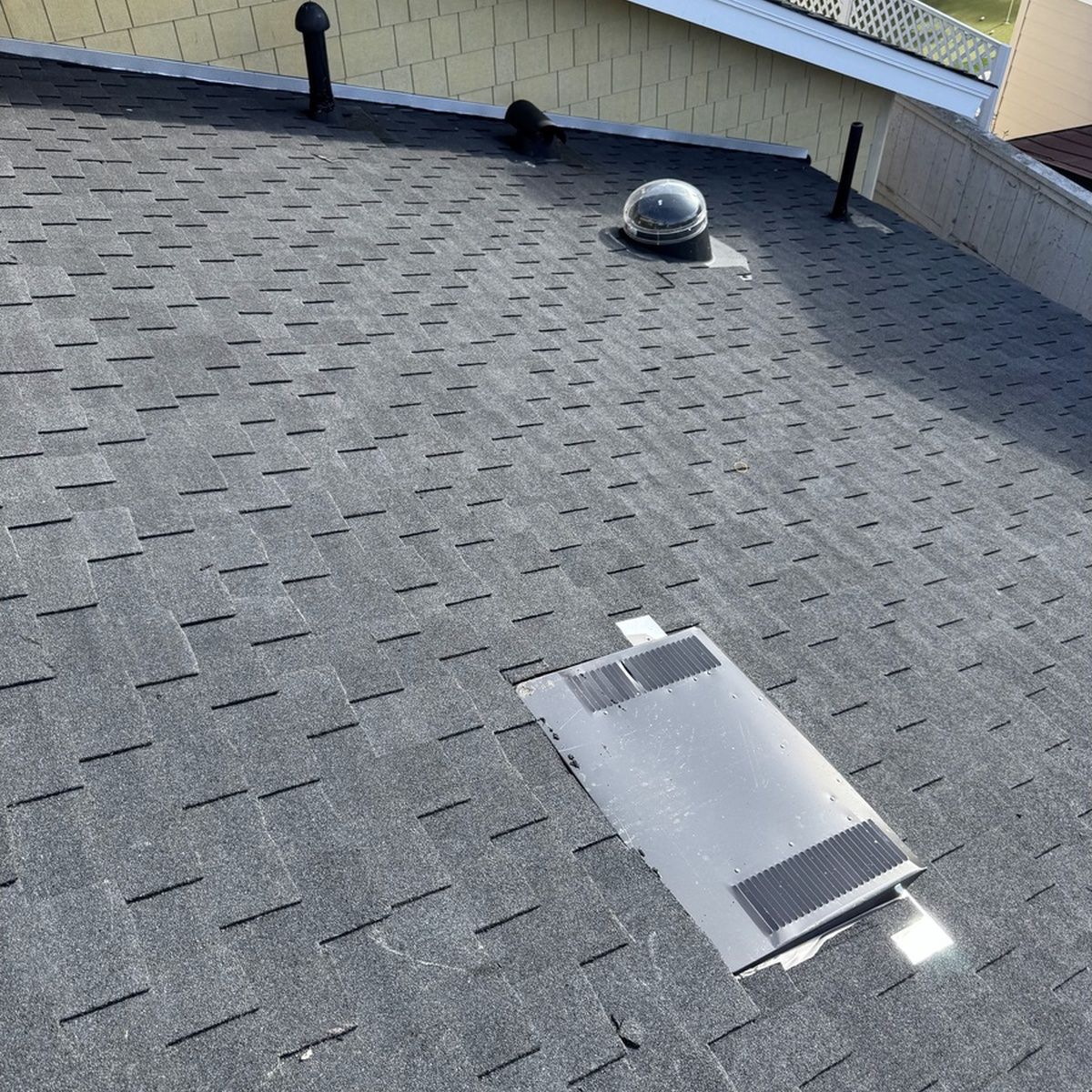 Rooftop with gray shingles, a small dome vent, and a rectangular skylight or roof hatch.