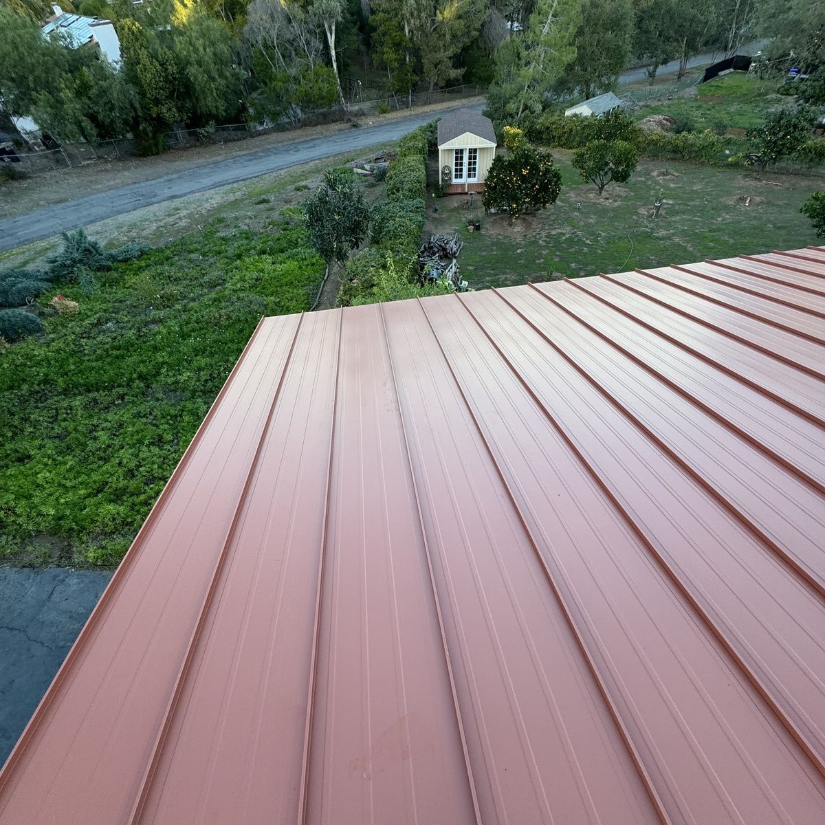 Red metal roof overlooking a grassy yard, small gazebo, and tree-lined roadside.
