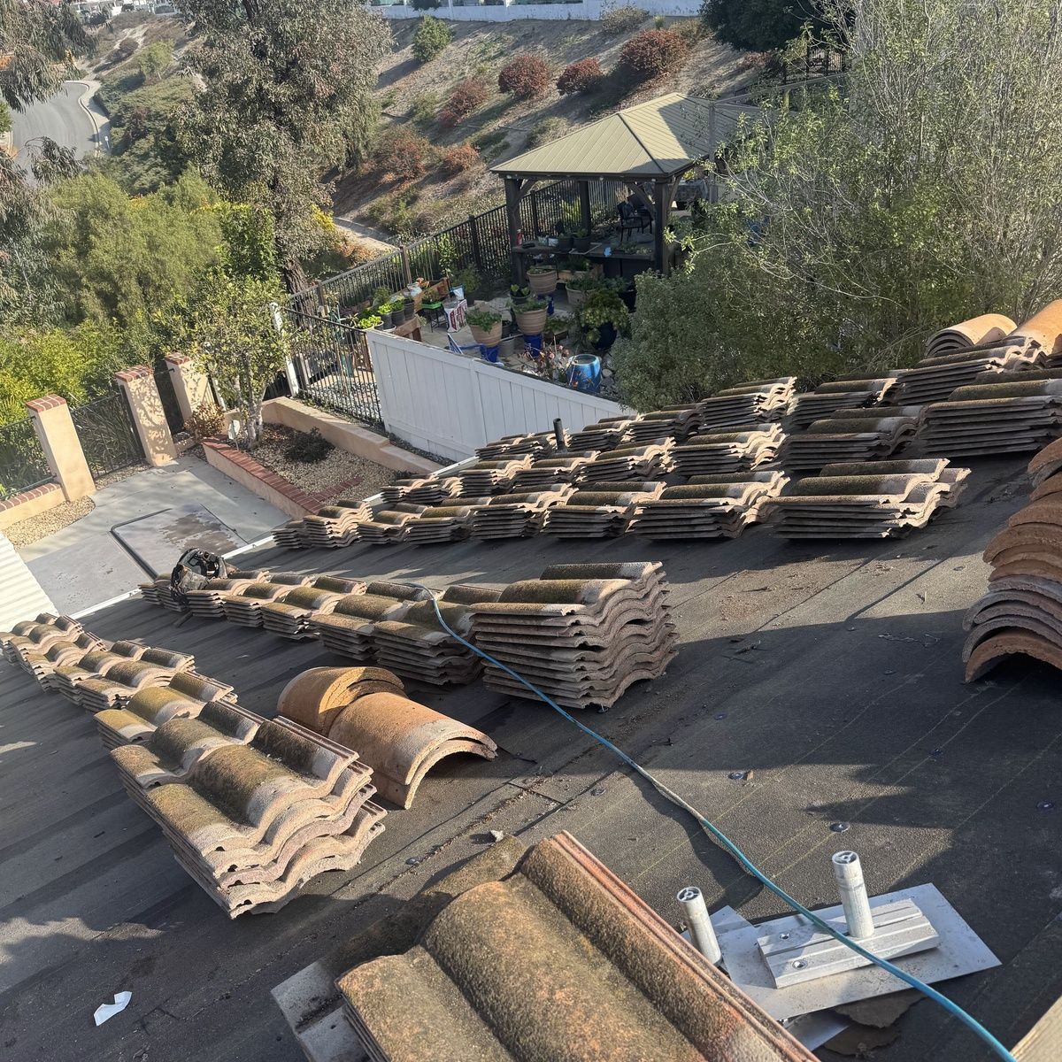 Stacked roof tiles on a sloped rooftop, with a gazebo and trees in the background.