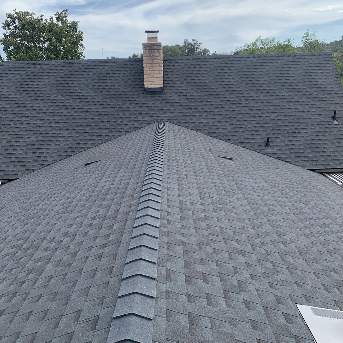 Gray shingled roof with a central chimney and ridge vent, viewed from above