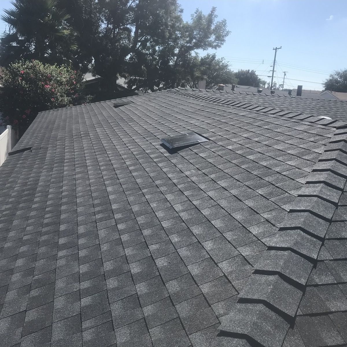 Gray shingled roof with a small vent, seen from above with trees in the background