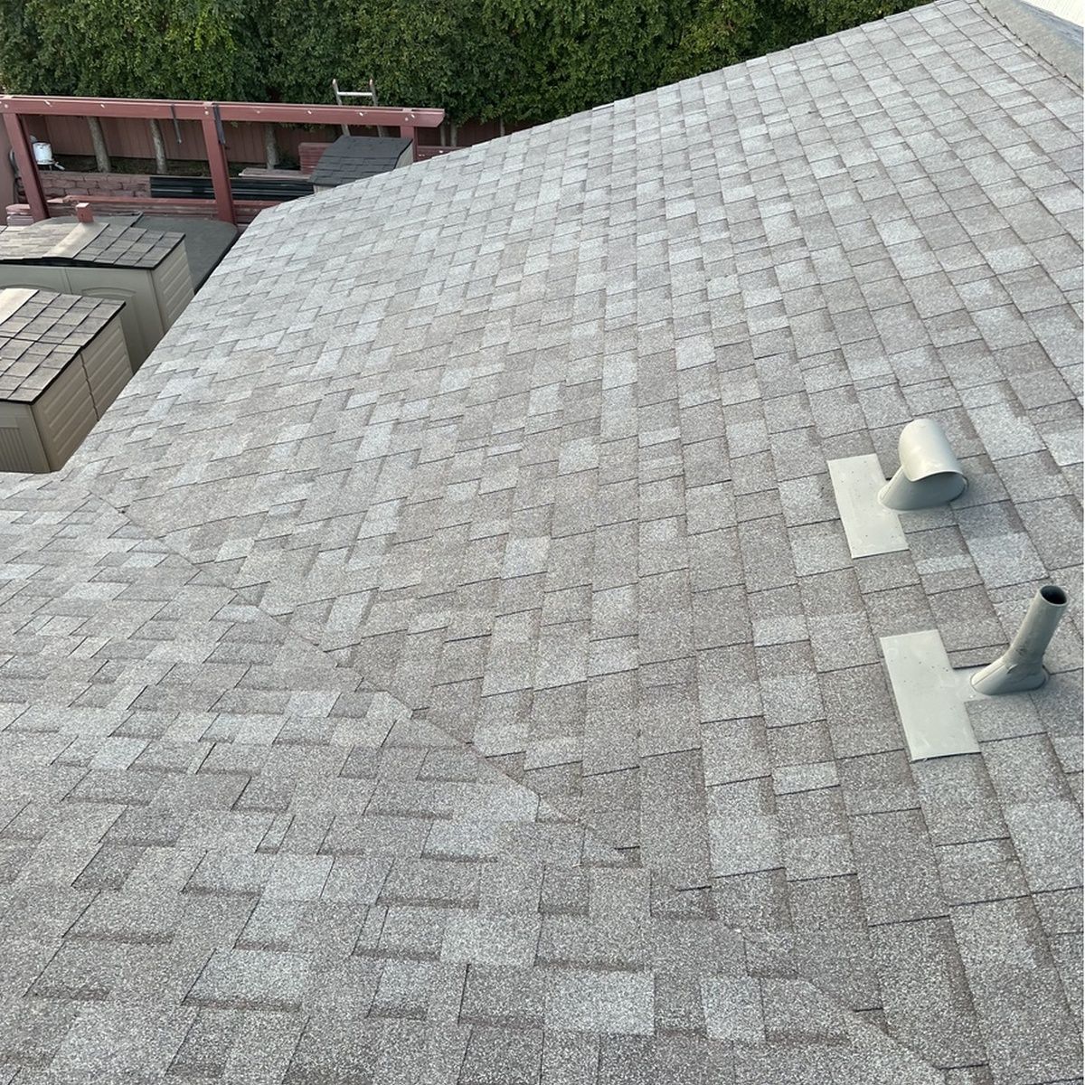 Gray shingled rooftop with two vent pipes and a red railing in the background